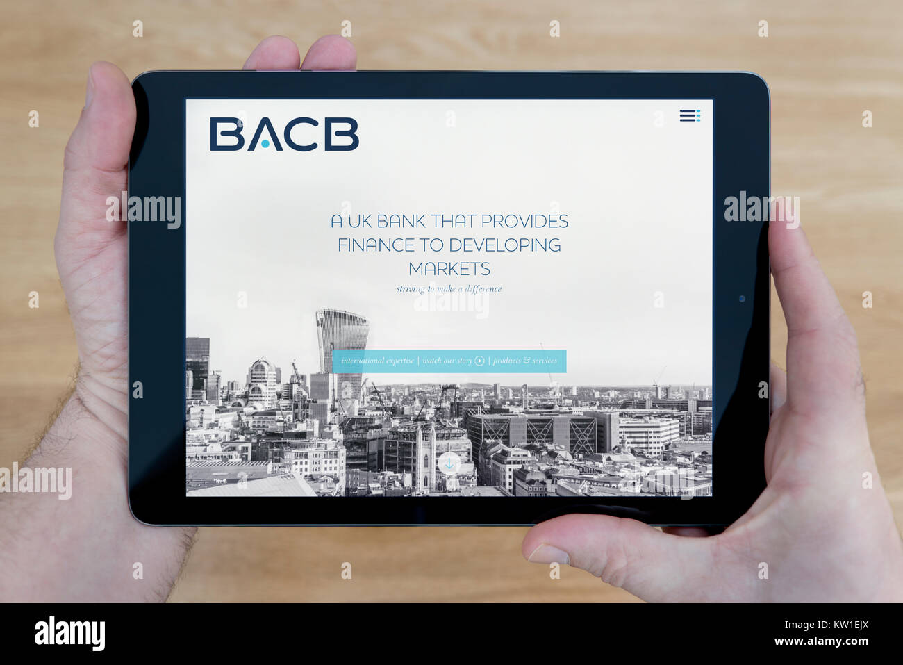 A man looks at the British Arab Commercial Bank (BACB) website on his iPad tablet device, shot against a wooden table top background (Editorial only) Stock Photo
