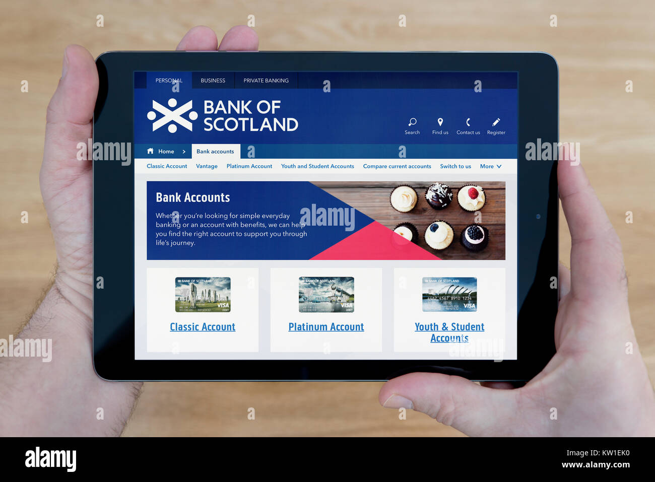 A man looks at the Bank of Scotland website on his iPad tablet device, shot against a wooden table top background (Editorial use only) Stock Photo