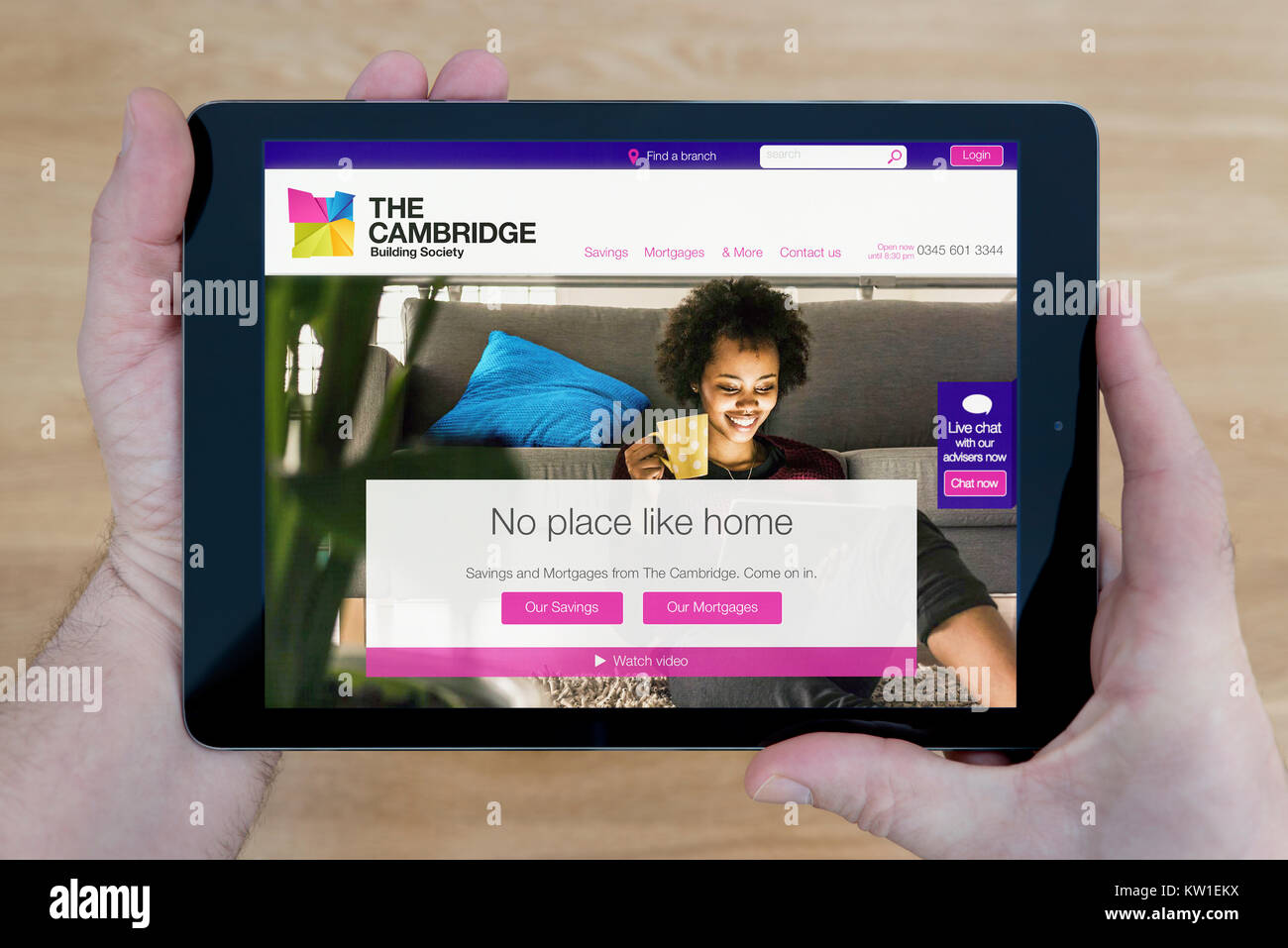 A man looks at the Cambridge Building Society website on his iPad tablet device, shot against a wooden table top background (Editorial use only) Stock Photo