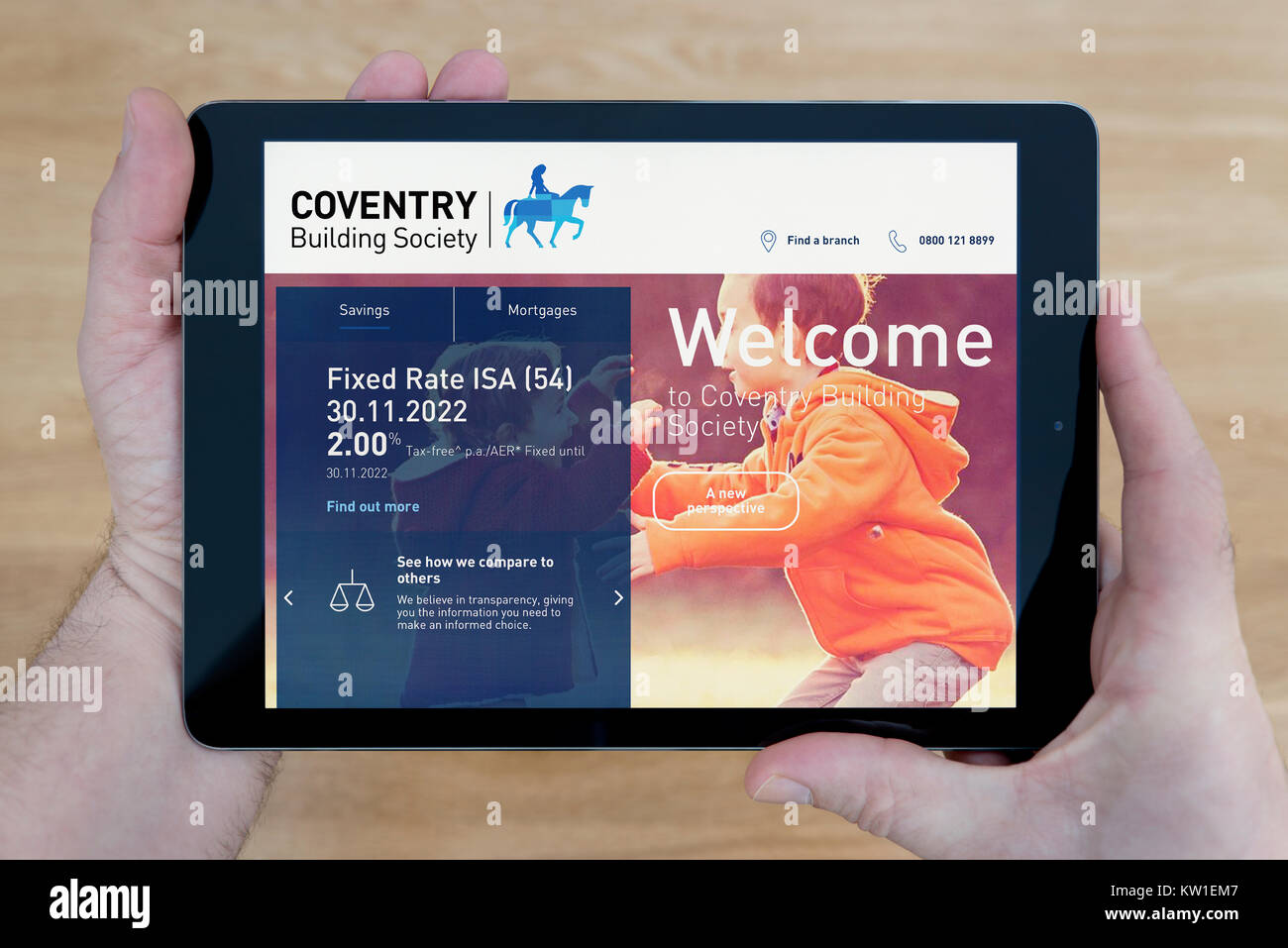 A man looks at the Coventry Building Society website on his iPad tablet device, shot against a wooden table top background (Editorial use only) Stock Photo