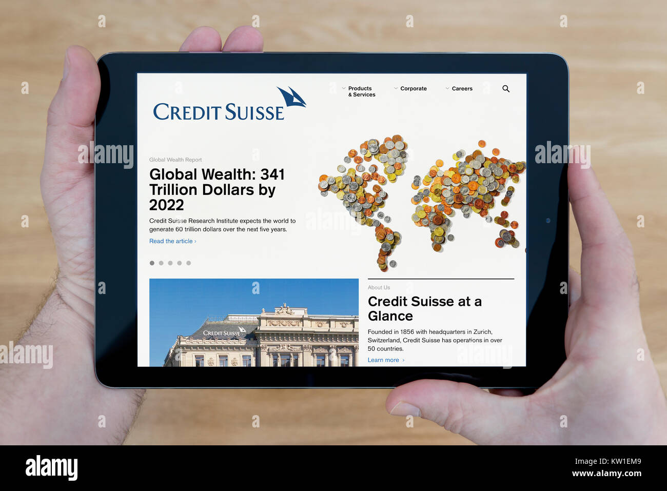 A man looks at the Credit Suisse Bank website on his iPad tablet device, shot against a wooden table top background (Editorial use only) Stock Photo