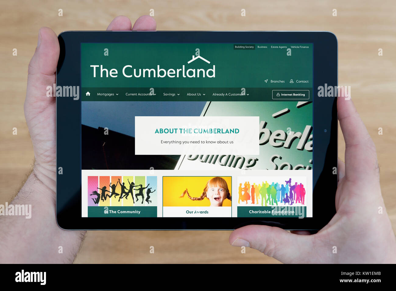 A man looks at the Cumberland Building Society website on his iPad tablet device, shot against a wooden table top background (Editorial use only) Stock Photo
