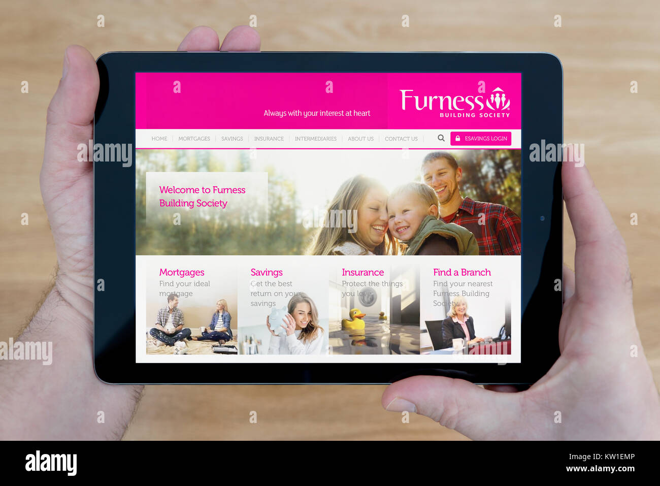 A man looks at the Furness Building Society website on his iPad tablet device, shot against a wooden table top background (Editorial use only) Stock Photo