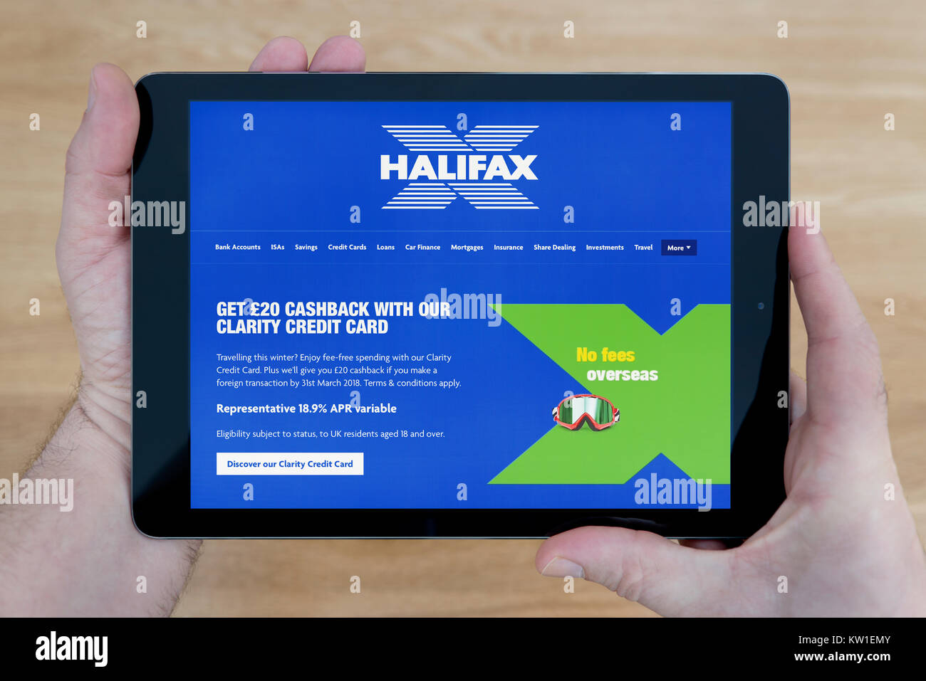 A man looks at the Halifax Building Society website on his iPad tablet device, shot against a wooden table top background (Editorial use only) Stock Photo