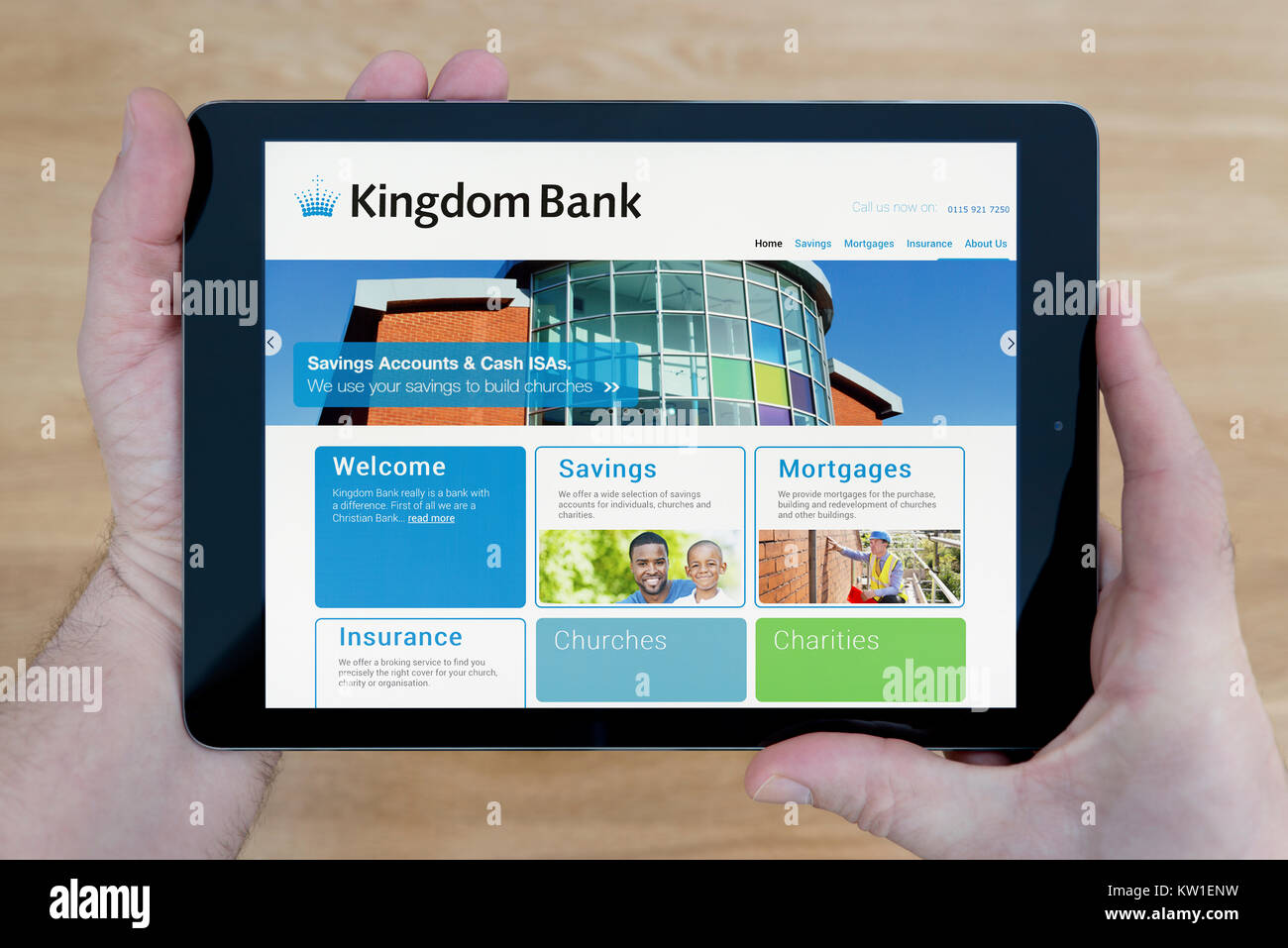 A man looks at the Kingdom Bank website on his iPad tablet device, shot against a wooden table top background (Editorial use only) Stock Photo