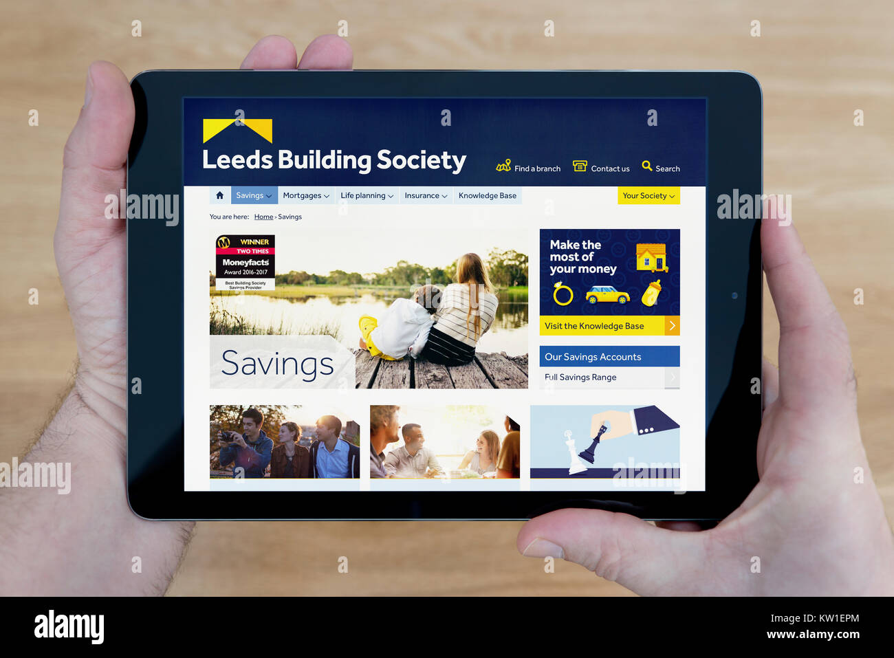 A man looks at the Leeds Building Society website on his iPad tablet device, shot against a wooden table top background (Editorial use only) Stock Photo