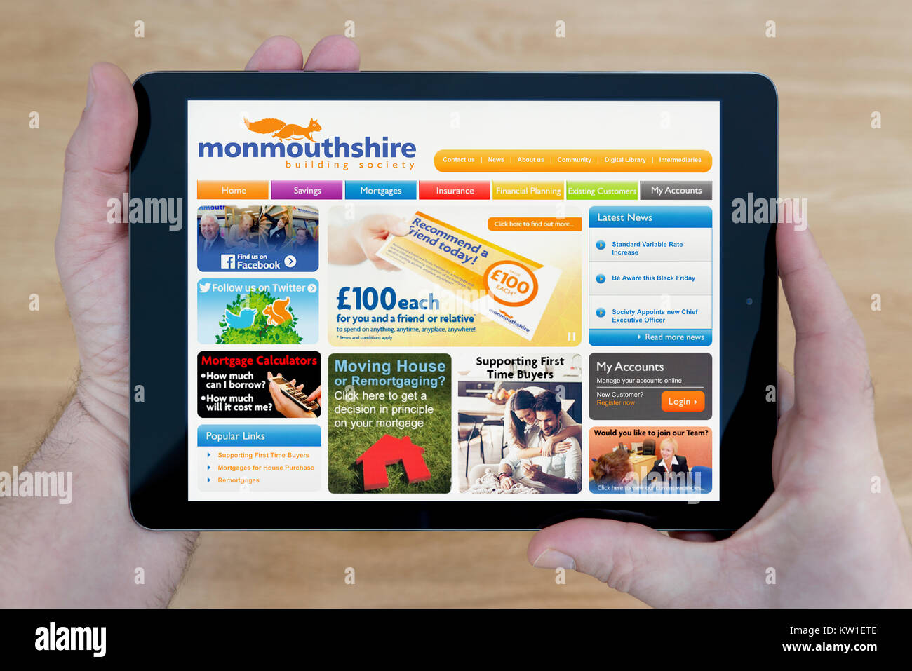 A man looks at the Monmouthshire Building Society website on his iPad tablet device, shot against a wooden table top background (Editorial use only) Stock Photo