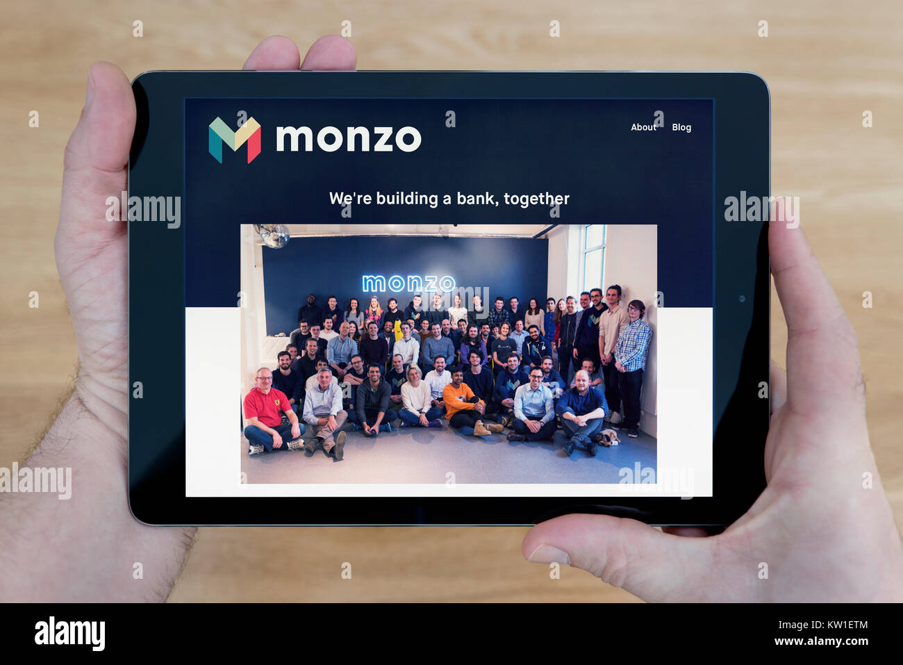 A man looks at the Monzo Bank website on his iPad tablet device, shot against a wooden table top background (Editorial use only). Stock Photo