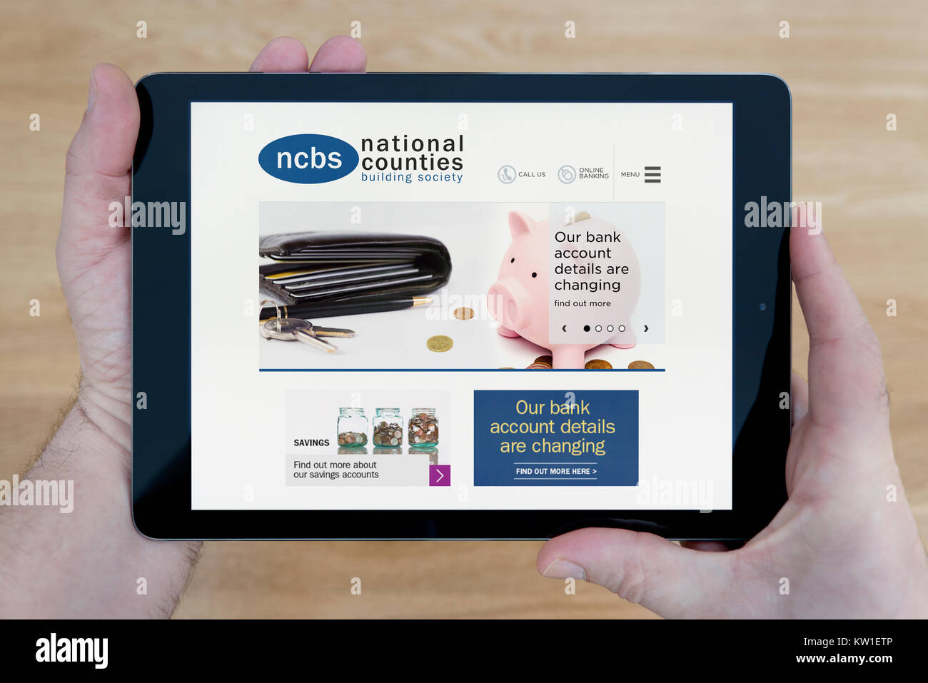 A man looks at the National Counties Building Society (NCBS) website on his iPad tablet, over a wooden table top background (Editorial use only) Stock Photo