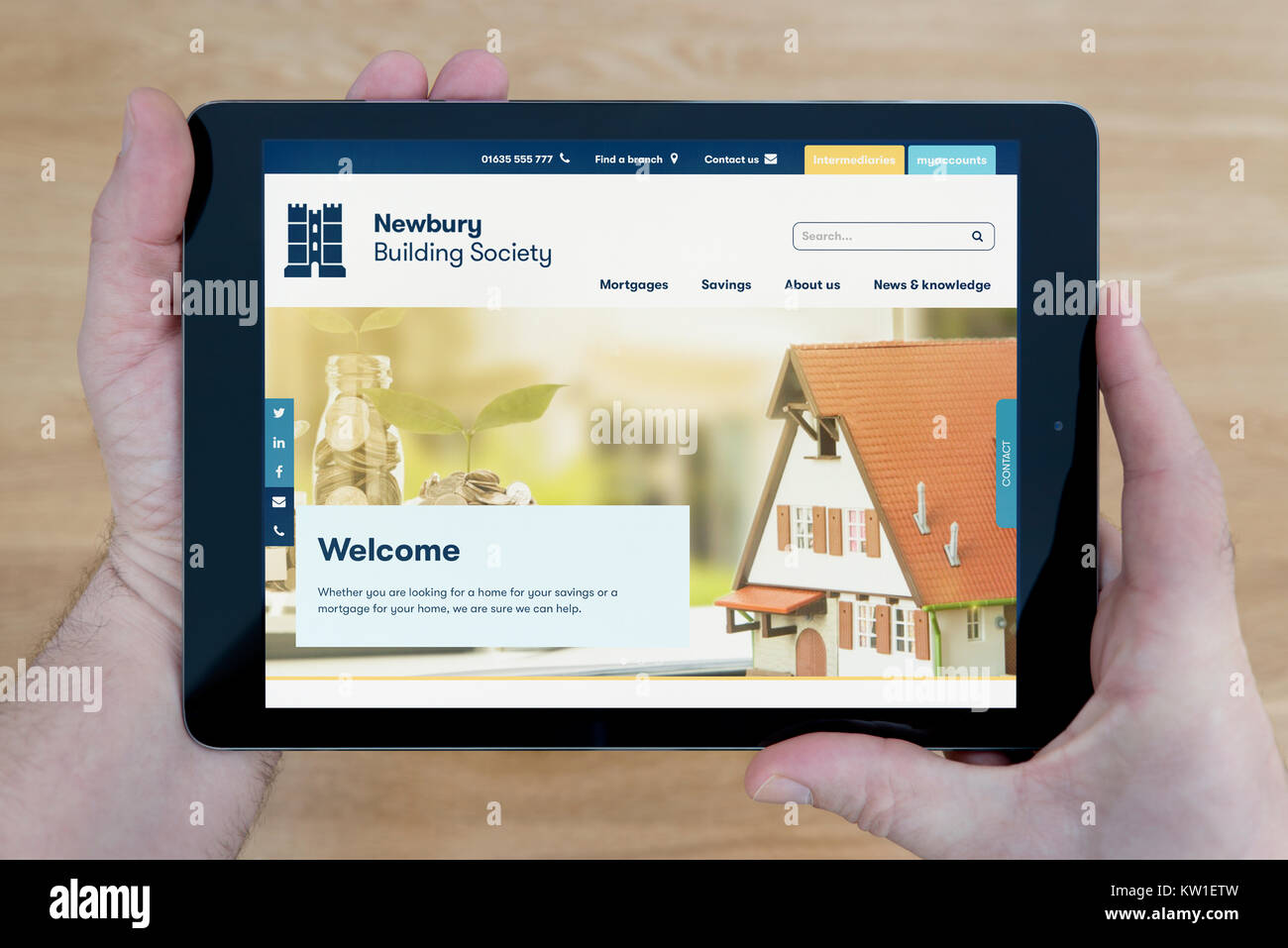 A man looks at the Newbury Building Society website on his iPad tablet device, shot against a wooden table top background (Editorial use only) Stock Photo