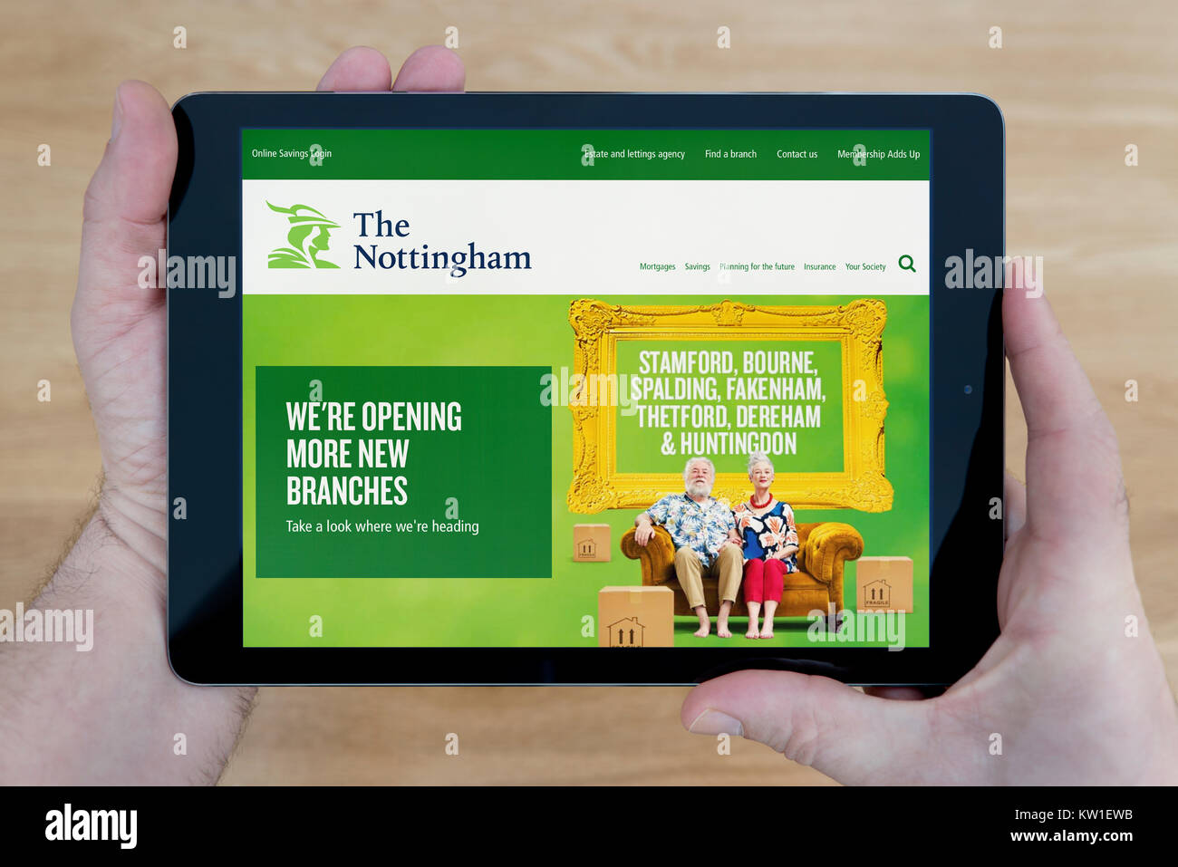 A man looks at the Nottingham Building Society website on his iPad tablet device, shot against a wooden table top background (Editorial use only) Stock Photo
