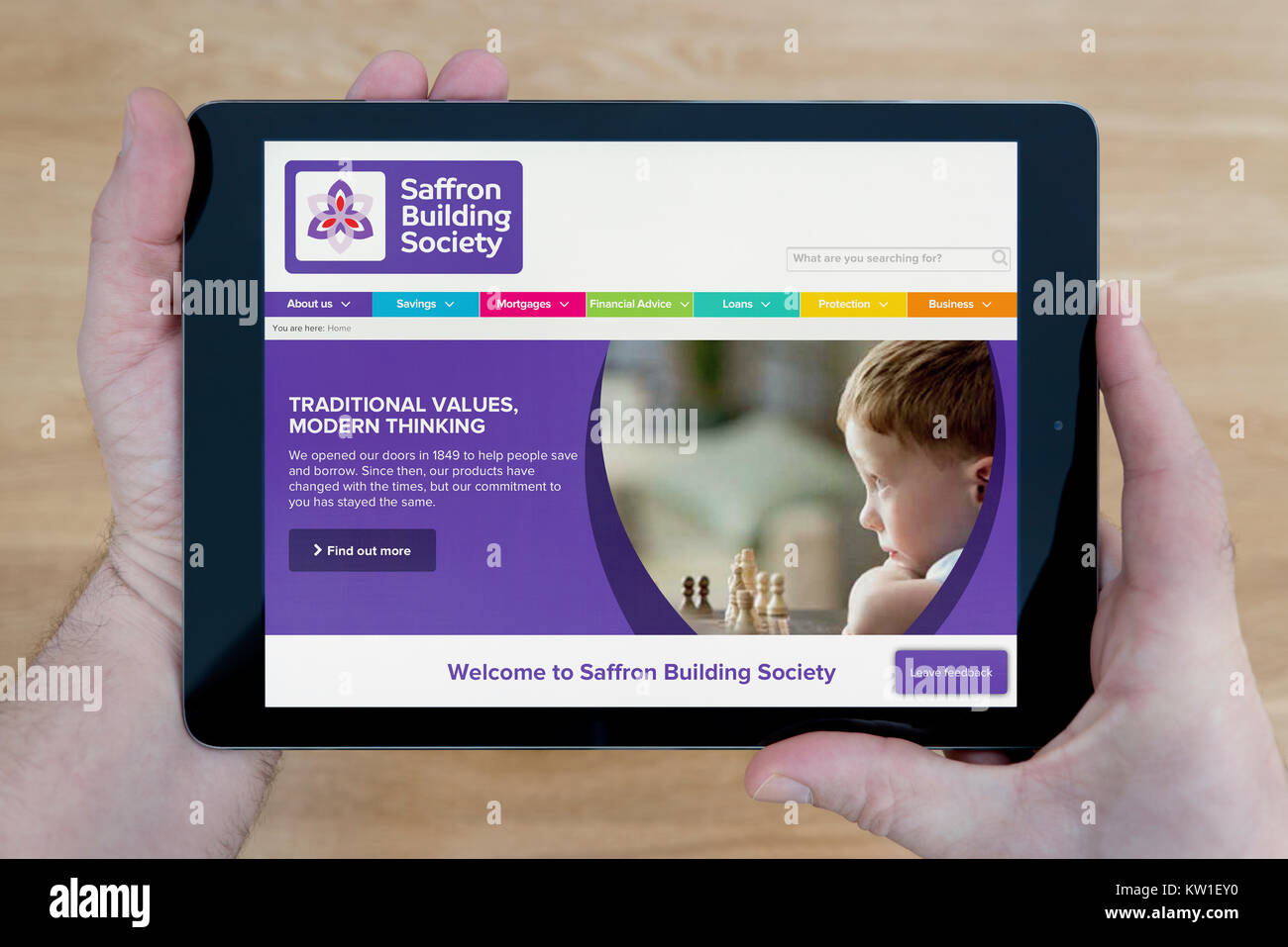 A man looks at the Saffron Building Society website on his iPad tablet device, shot against a wooden table top background (Editorial use only) Stock Photo
