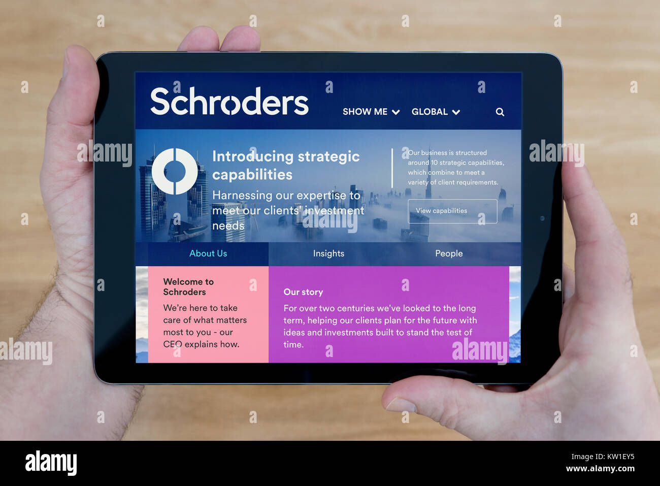 A man looks at the Schroders website on his iPad tablet device, shot against a wooden table top background (Editorial use only) Stock Photo