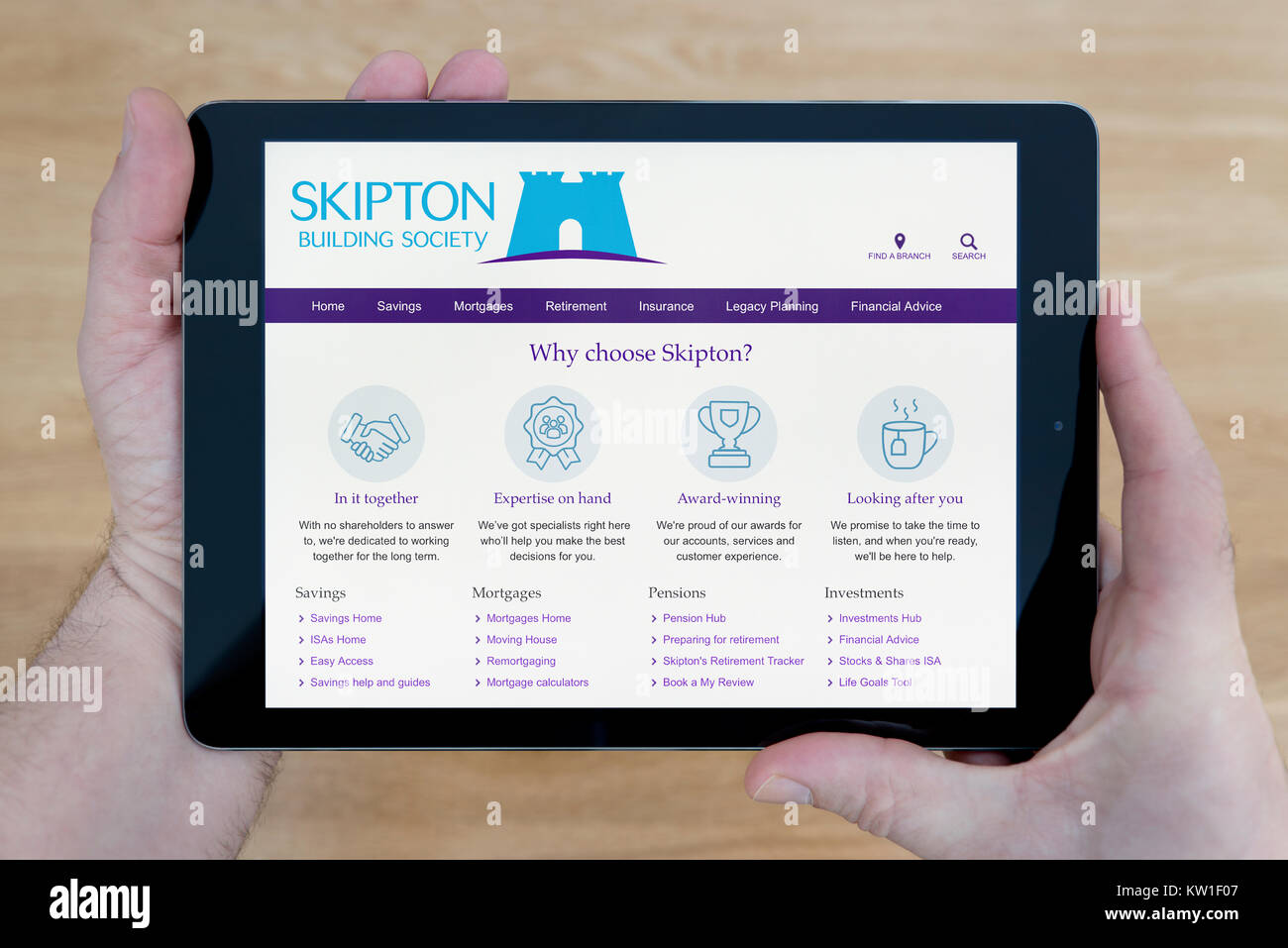 A man looks at the Skipton Building Society website on his iPad tablet device, shot against a wooden table top background (Editorial use only) Stock Photo