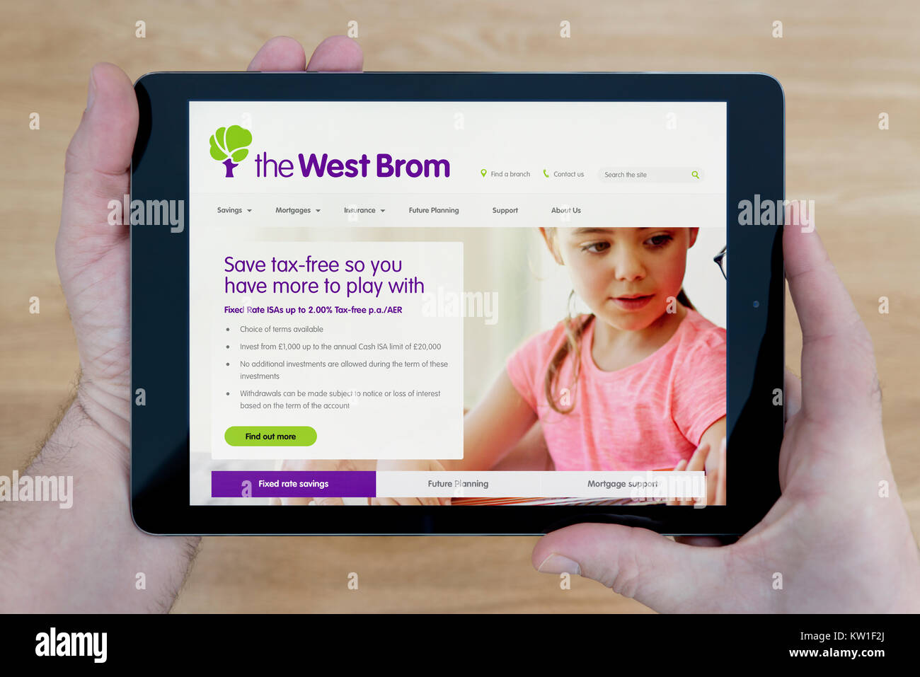 A man looks at the West Brom Building Society website on his iPad tablet device, shot against a wooden table top background (Editorial use only) Stock Photo
