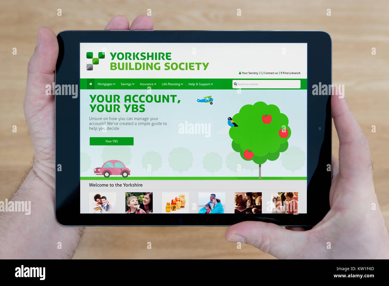 A man looks at the Yorkshire Building Society website on his iPad tablet device, shot against a wooden table top background (Editorial use only) Stock Photo
