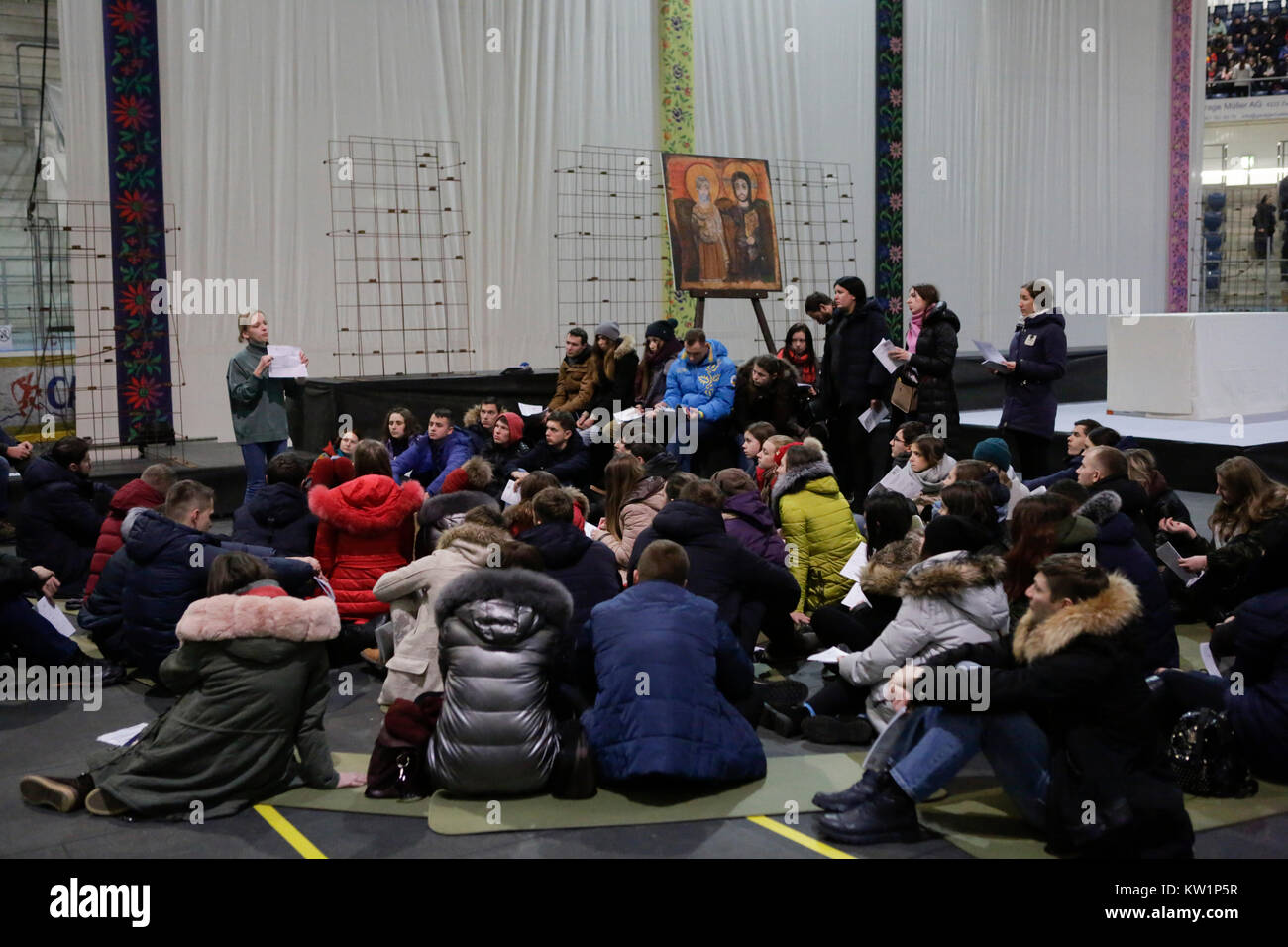 Basel, Switzerland. 28th Dec, 2017. Volunteers sit together on the ground and listen to the explanations about the general rules of the meeting and the plans for the days in Basel. Several thousand young pilgrims from all over Europe and beyond arrived in Basel in Switzerland for the annual European Youth Meeting of the ecumenical Taize community. The meeting of prayers and meditation is held under the motto 'Pilgrimage of Trust on Earth' and is the 40th anniversary meeting. Credit: Michael Debets/Alamy Live News Stock Photo