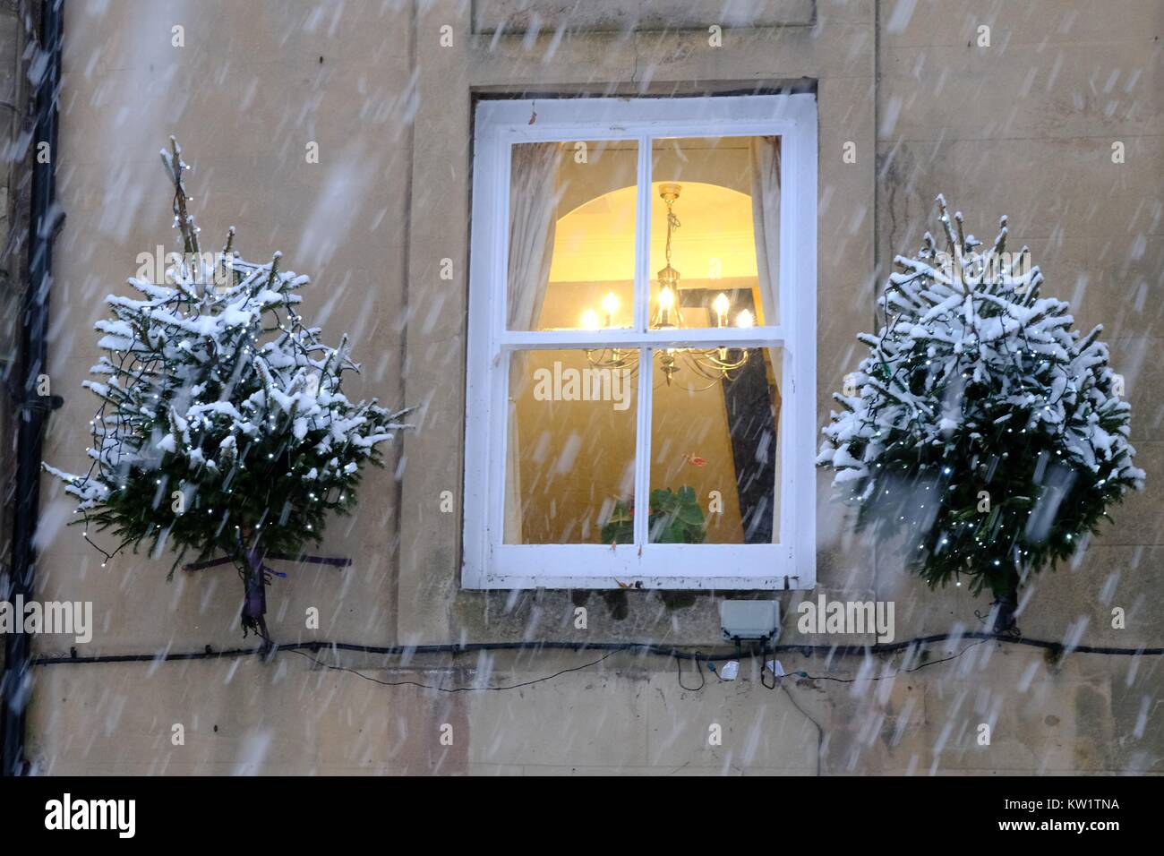 Buxton, Derbyshire. Christmas trees and light in window with falling snow in the Peak District