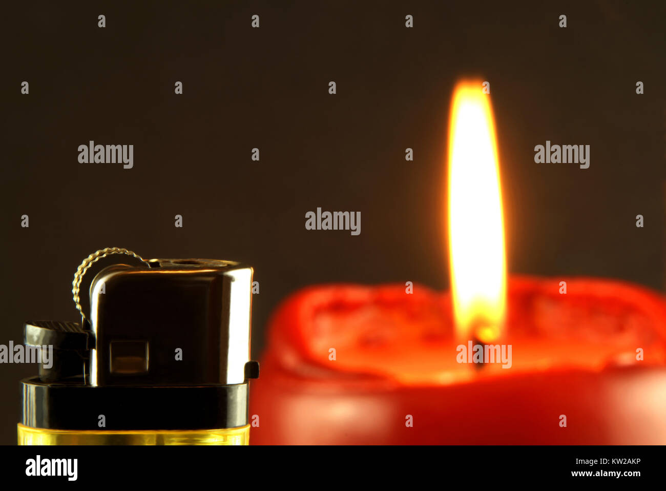Closeup of a lighter with burning candle in front of dark background Stock Photo