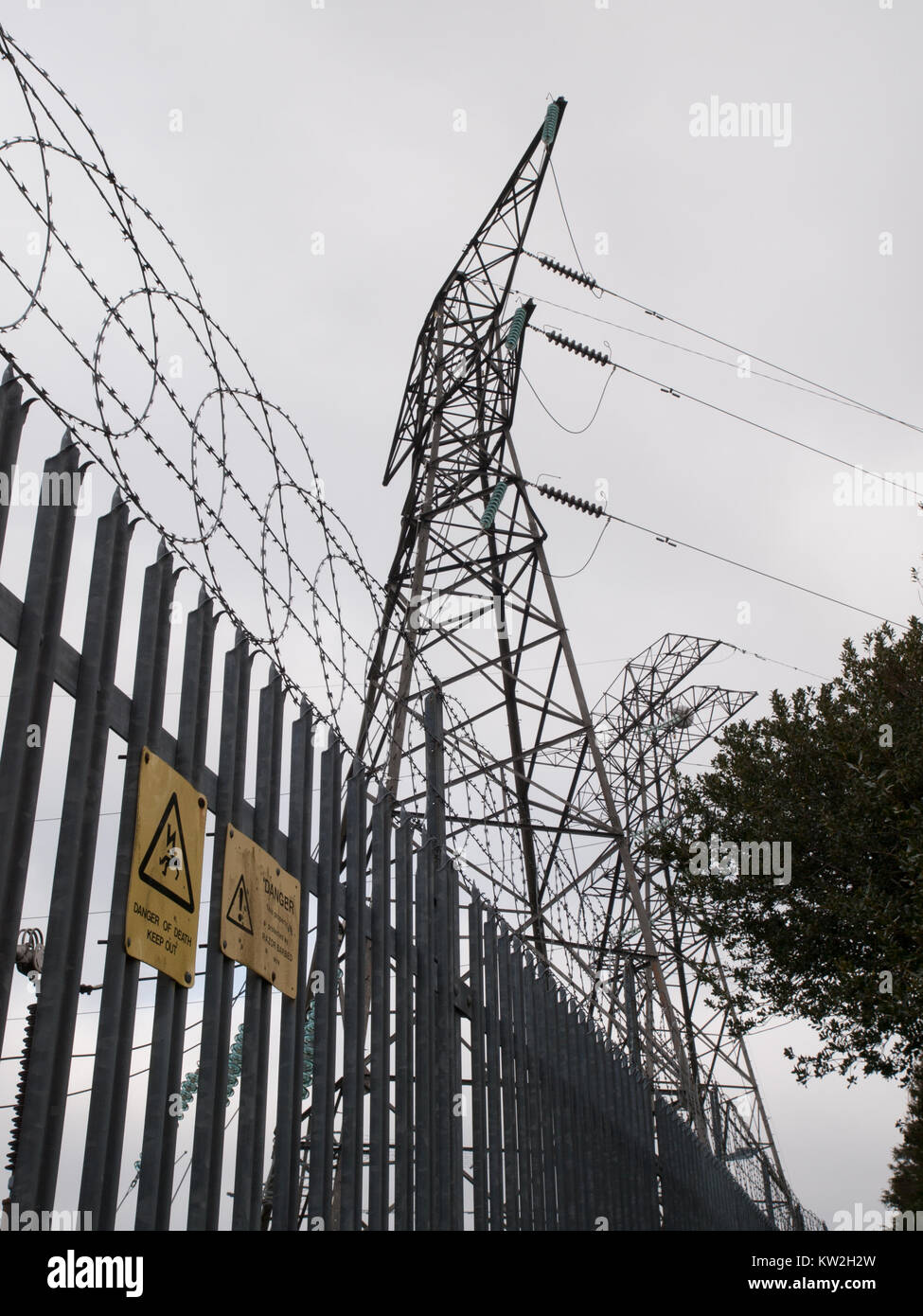 Electricity pylons behind razor wire security fence with warning signs Stock Photo