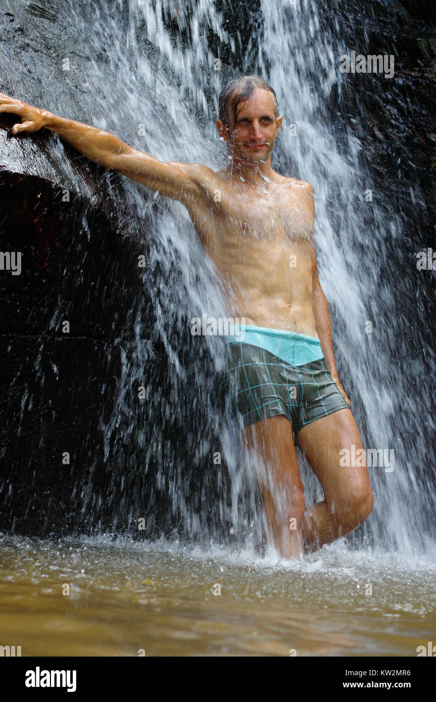 a man taking a relaxing shower under a waterfall outside Stock Photo