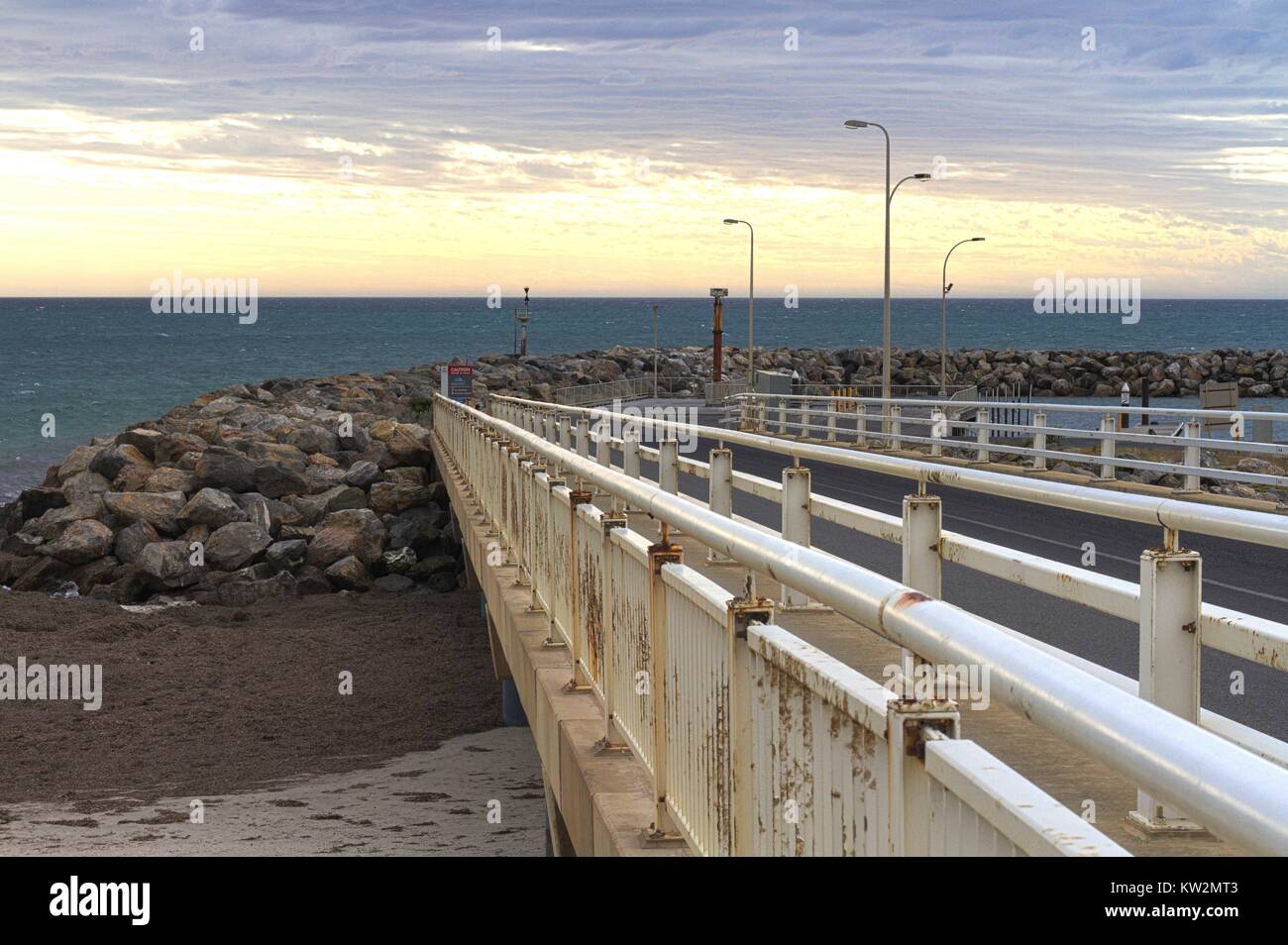 Concrete pier leading out to a rocky breakwater, view of the ocean and sunset. Stock Photo
