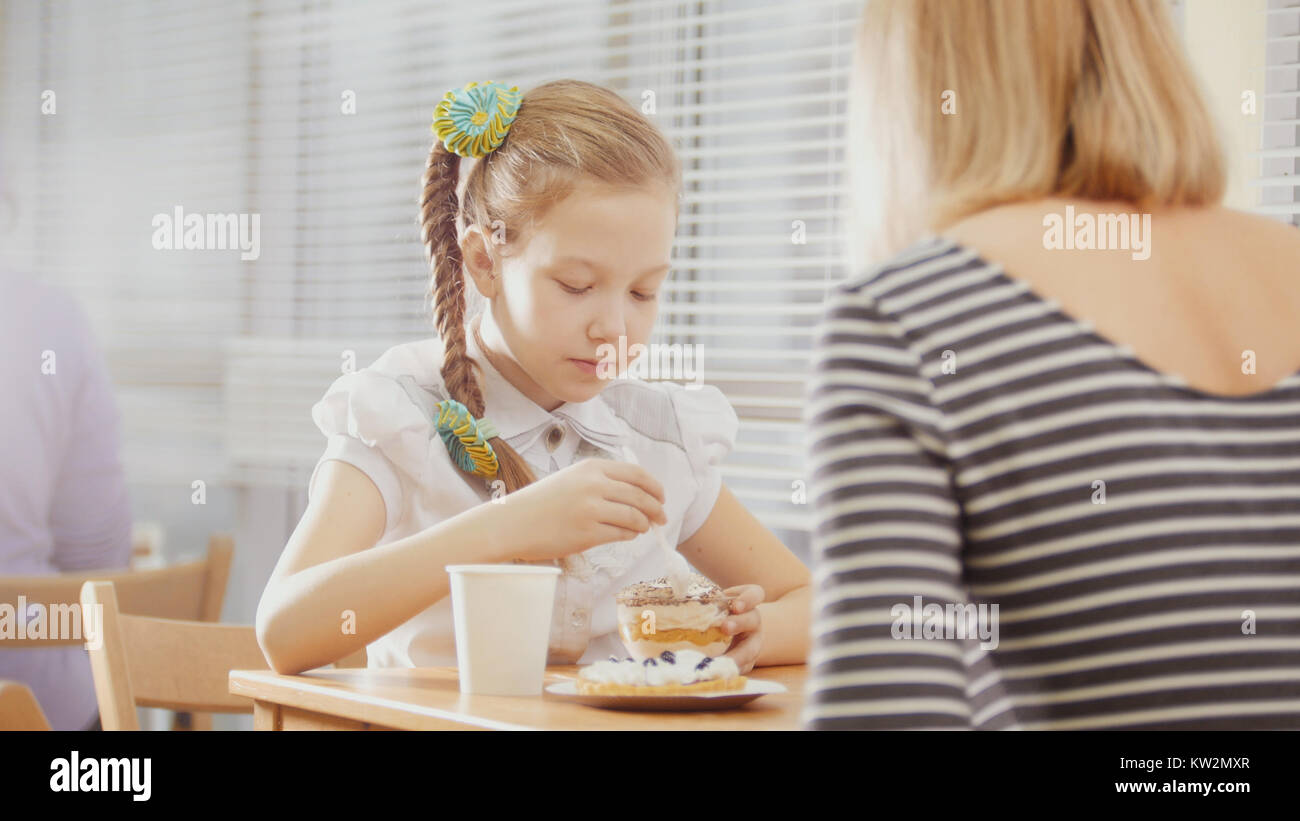 Mother and daughter eating breakfast at the table. On the table cakes. Stock Photo