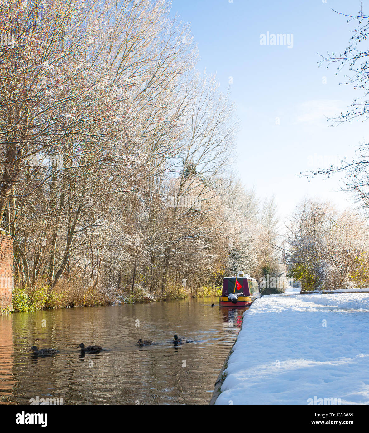 British canals in winter. UK narrowboat moored alongside snow-covered towpath in morning sunshine. Canal boat life in the snow. Stock Photo