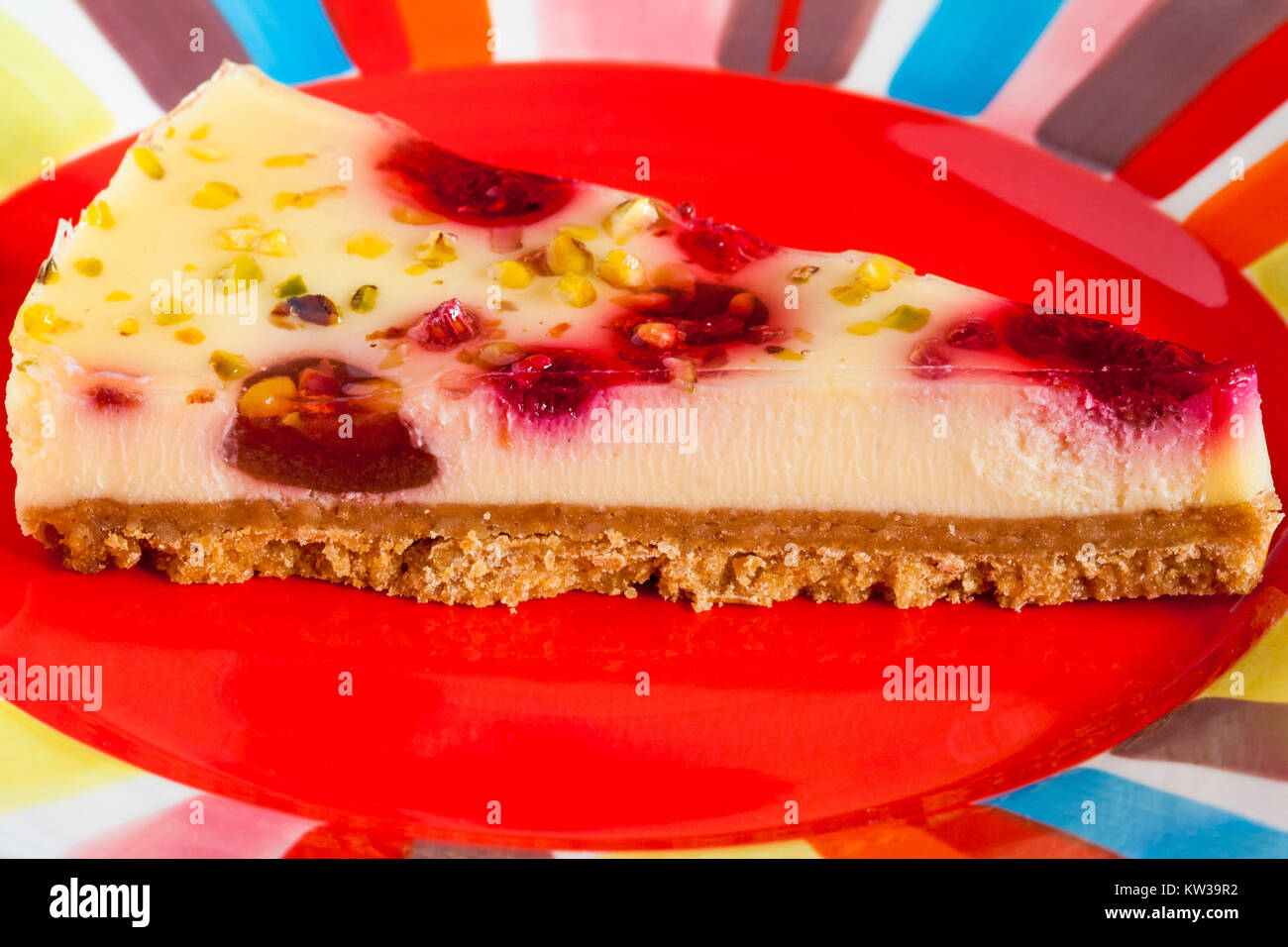 Tesco finest Raspberry & Pistachio cheesecake slice on red colourful plate Stock Photo