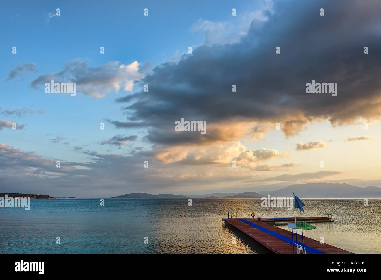 Sunrise with fluffy clouds on a golden blue sky over calm sea with an L shaped wooden pier Stock Photo