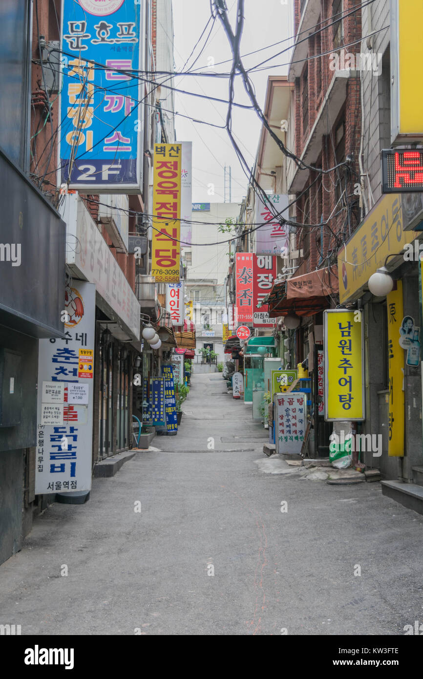 A long narrow alley way with colorful signs to shops and restaurants, on both sides, with cables and wires overhead, in Seoul, South Korea Stock Photo