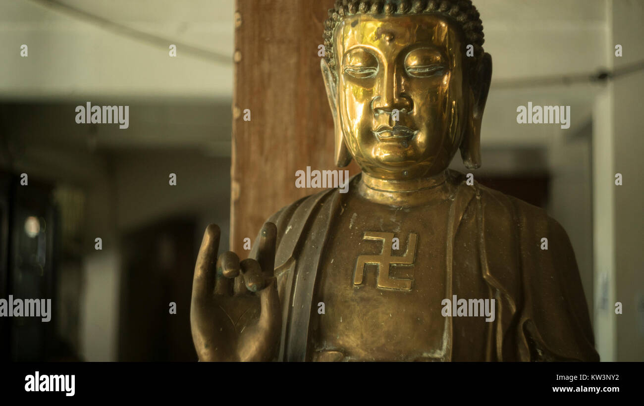 Buddha statue. More unusual counter-clockwise swastika symbolizes the auspicious footprints of the Buddha. Karana Mudra hand gesture: expelling demons Stock Photo