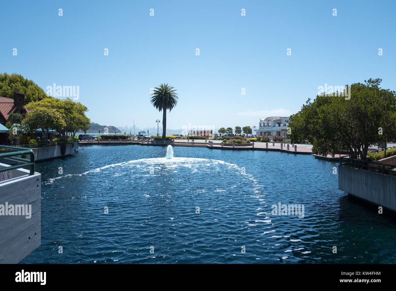 Fountains and palm trees are visible around Tiburon Lagoon, with San Francisco Bay and the shops along Main Street in the background, Tiburon, California, 2016. Stock Photo