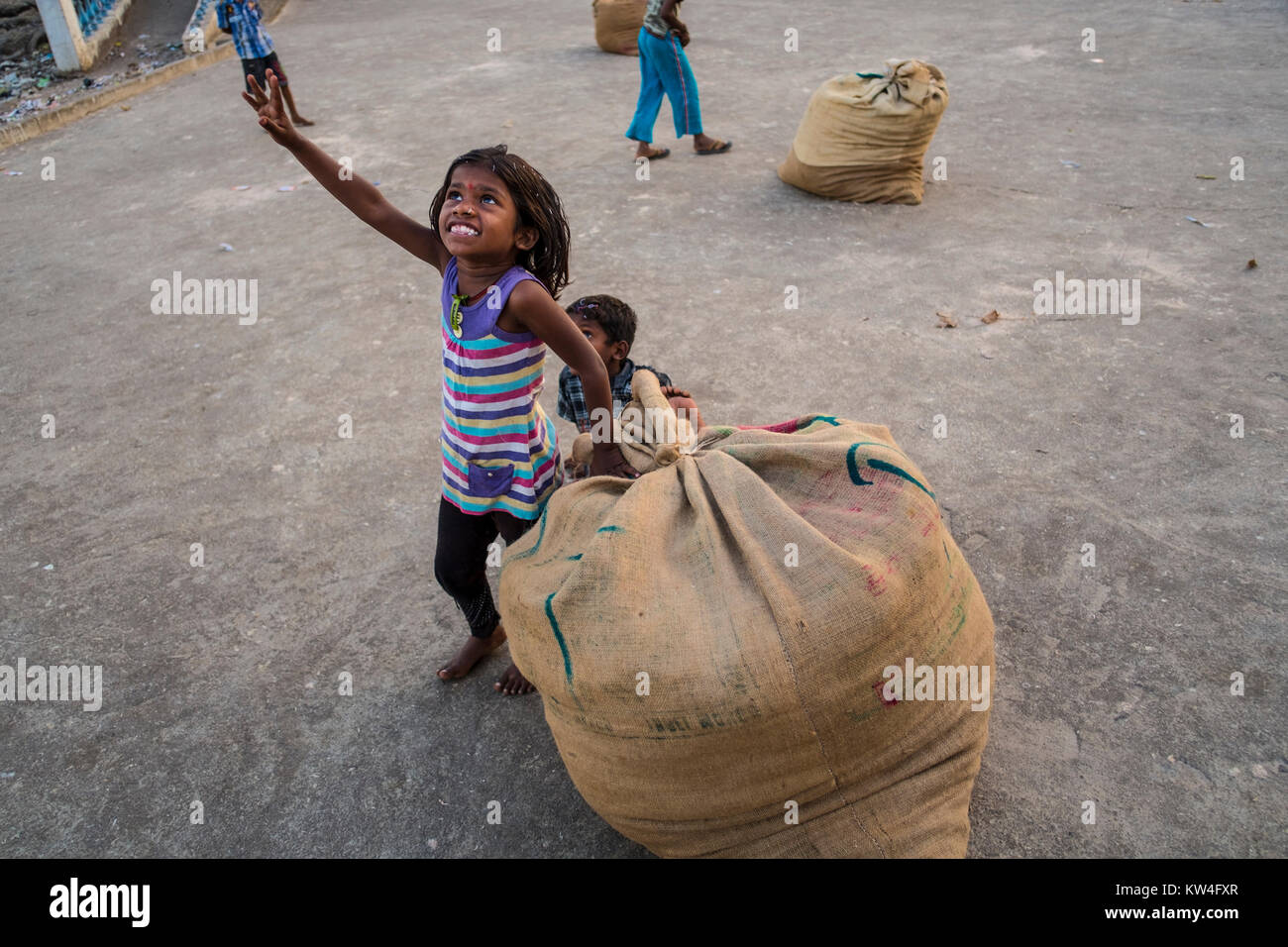 A little girl gets all excited looking at a airplane flyimng overhead as she manages a large gunny sack of dried fish. Stock Photo