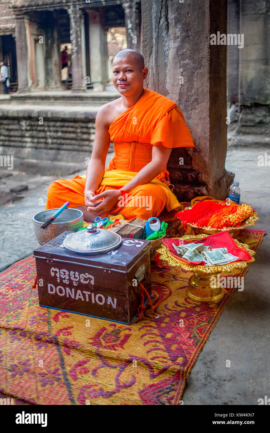 A Buddhist monk dressed in traditional saffron robe gives blessings to tourists who donate to his order. American dollars fill his donation bowl. USA  Stock Photo