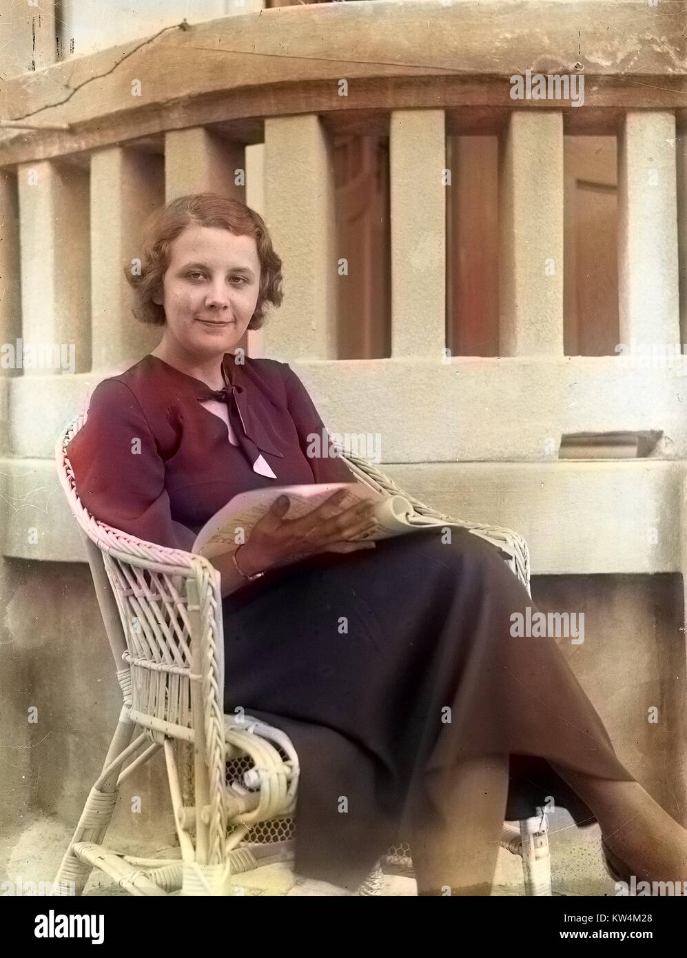 Portrait of a young, pretty woman sitting in a wicker chair outdoors ...