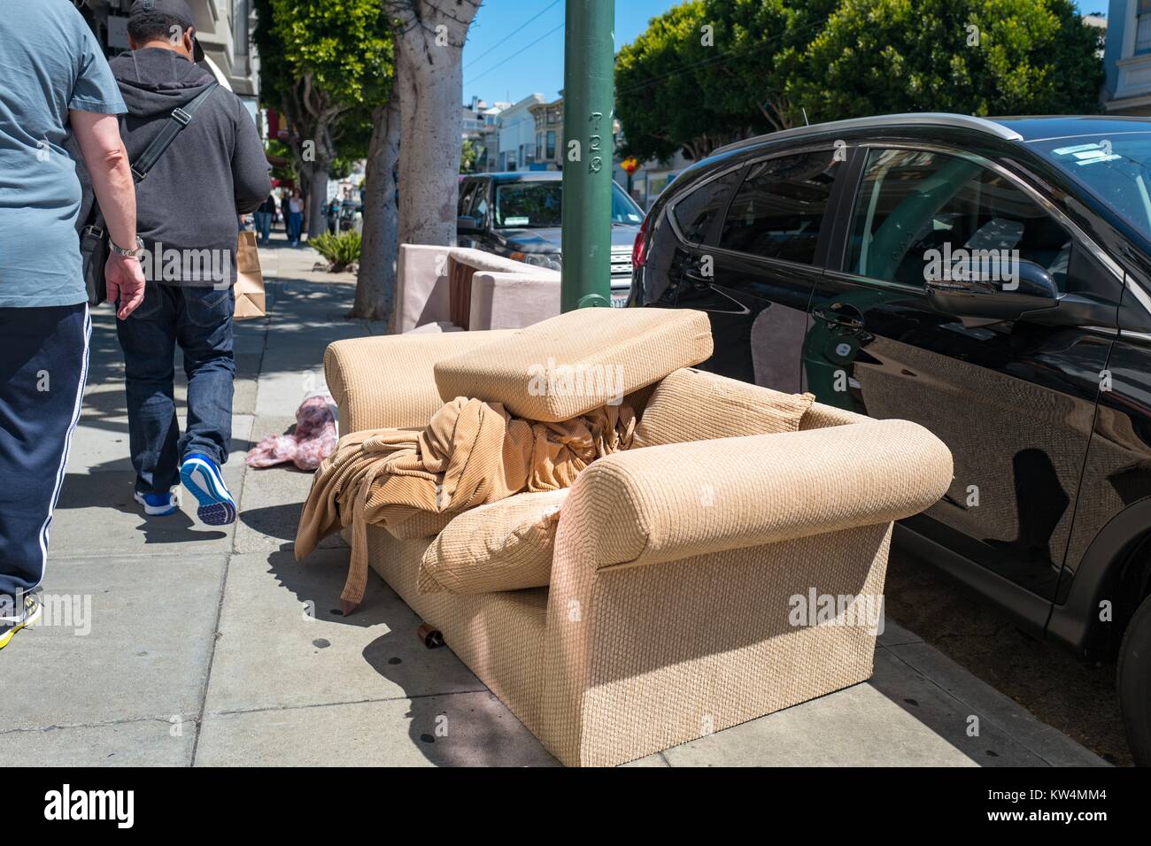 Residents walk past a beige couch which has been abandoned on the side of the road in the Cow Hollow neighborhood of San Francisco, California, August 28, 2016. Stock Photo
