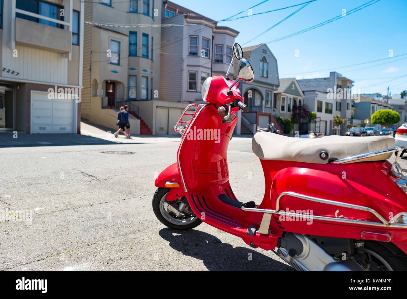 A bright red Vespa scooter parked on the street on a sunny day in the