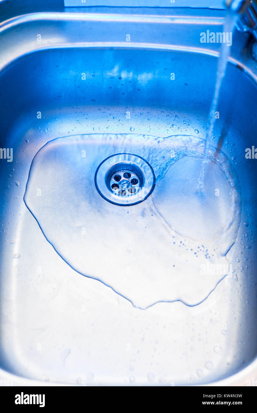 A stream of clean water flows into the stainless steel sink in blue