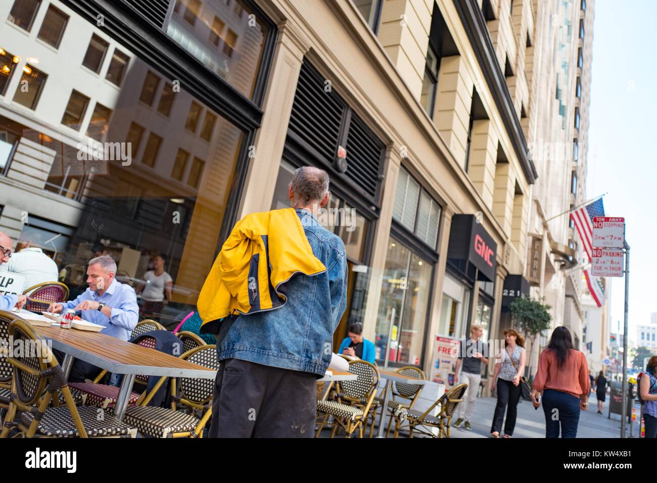 A homeless man wearing a denim jacket approaches a well-dress man in a button down shirt as he eats lunch at a restaurant in the Financial District neighborhood of San Francisco, California, September 26, 2016. Stock Photo