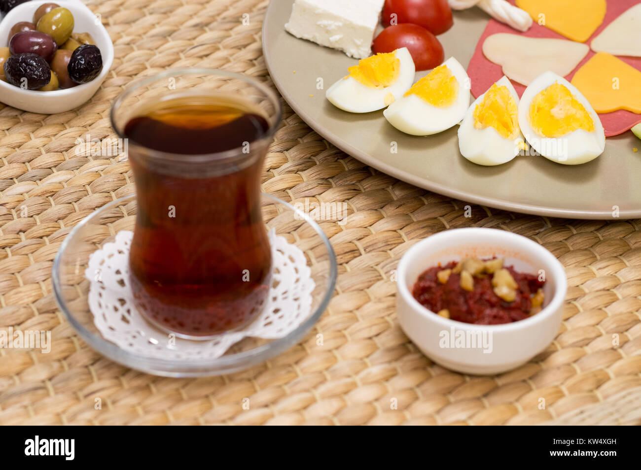 Close up of blurred traditional Turkish tea and appetizer with breakfast served on porcelain plate with cheese, salami, boiled egg, and tomato. Stock Photo