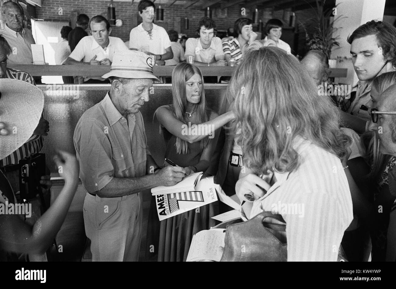 Bing Crosby, the famous American singer and actor, is pictured signing autographs, engaging with his fans. This photograph captures his popularity and connection with his audience during his career's peak. Stock Photo