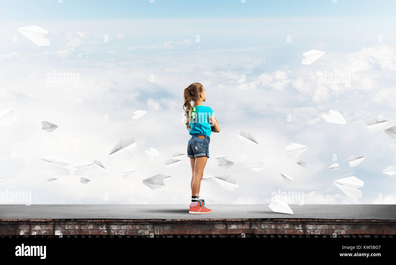 Cute kid girl standing on building roof and paper planes flying around ...