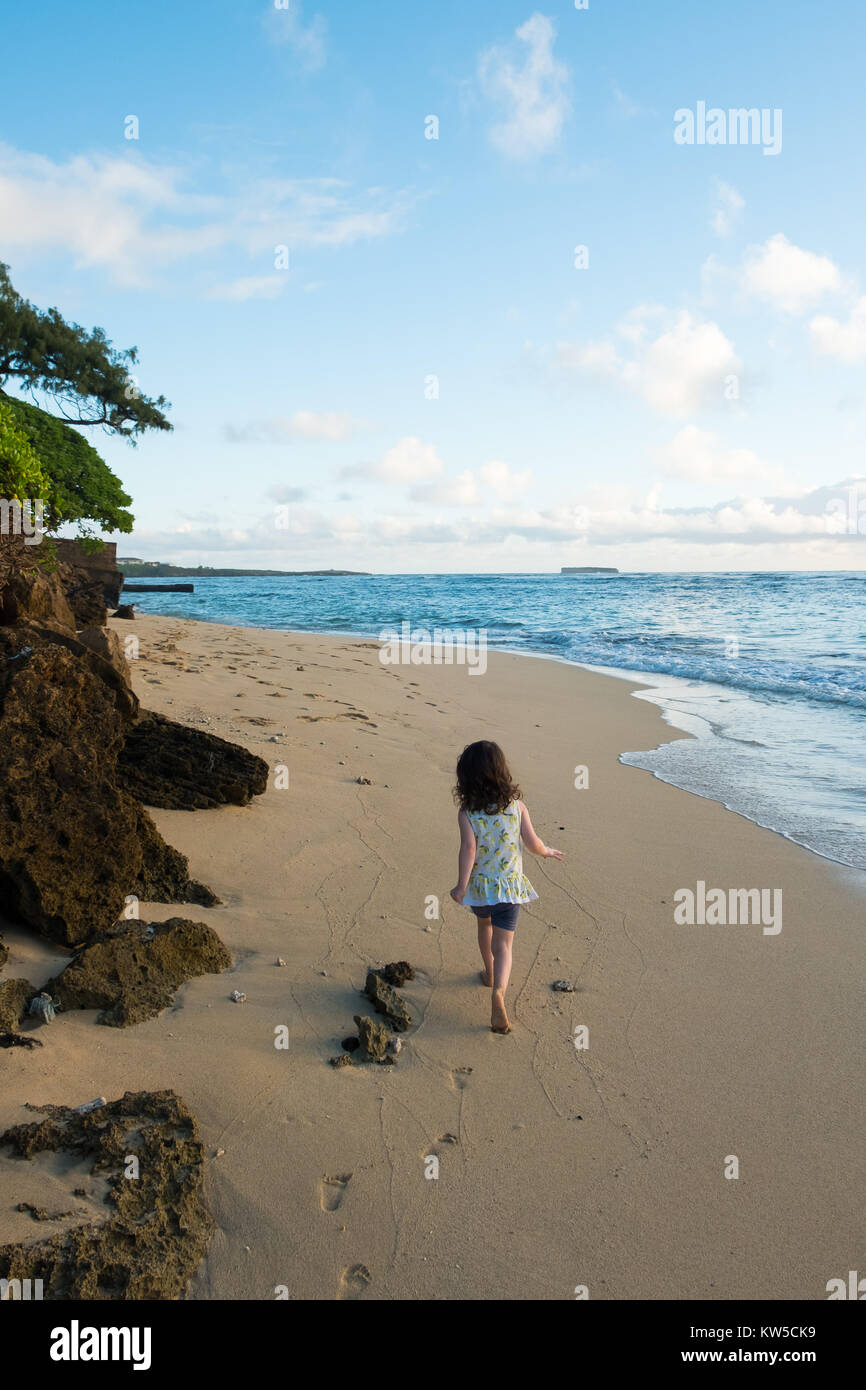 Little girl running on the beach at sunrise while having fun on vacation in Oahu Hawaii. Stock Photo