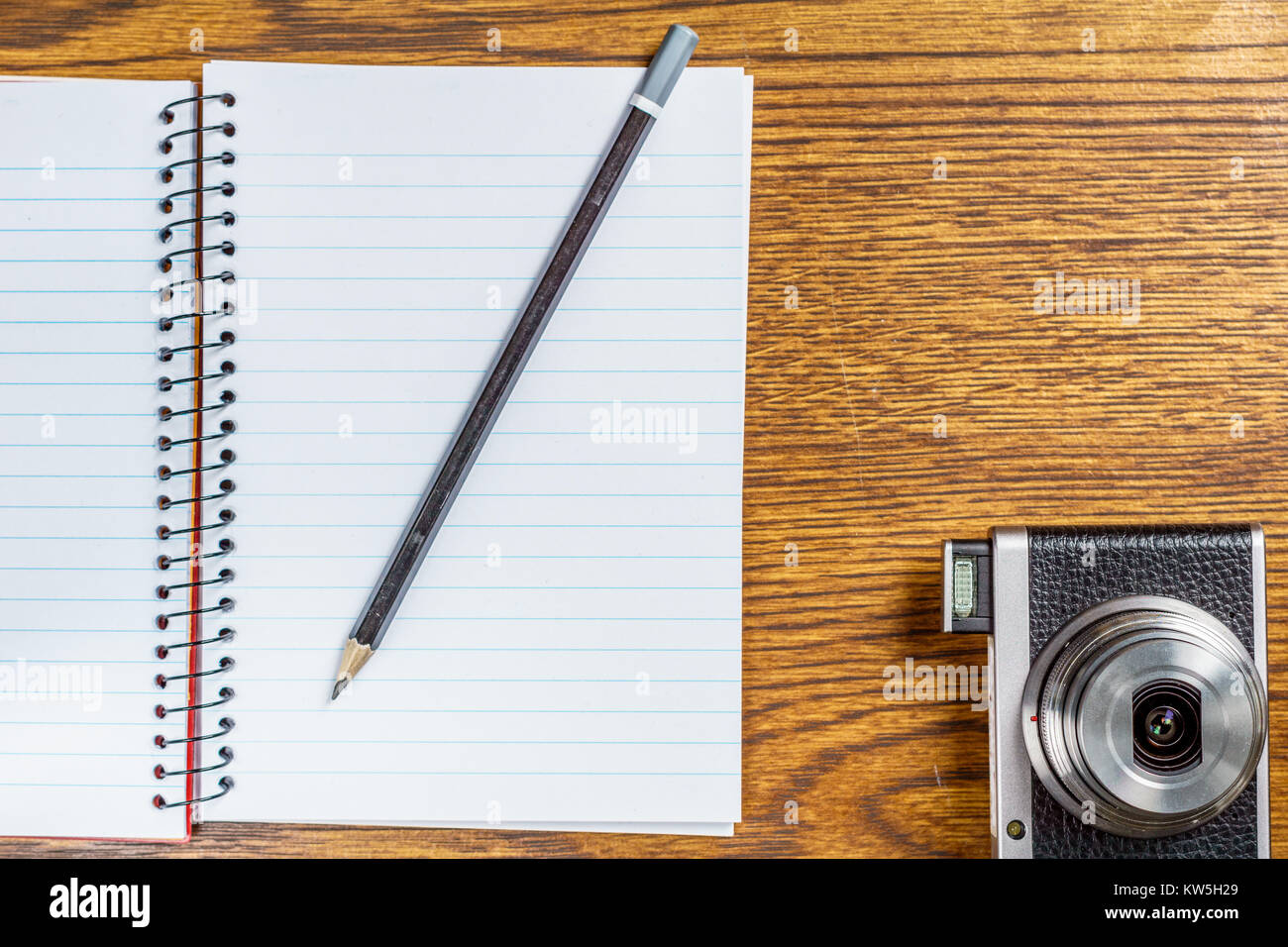 Top view of open spiral notebook with black pencil and photo camera on ...