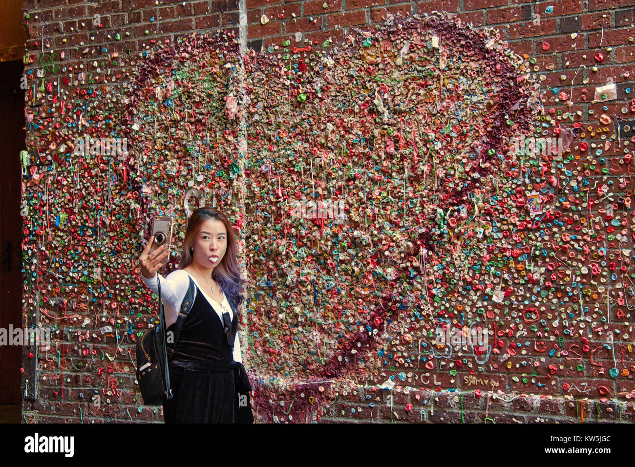Asian woman taking selfie in front of the gum wall, Seattle, Washington, USA Stock Photo