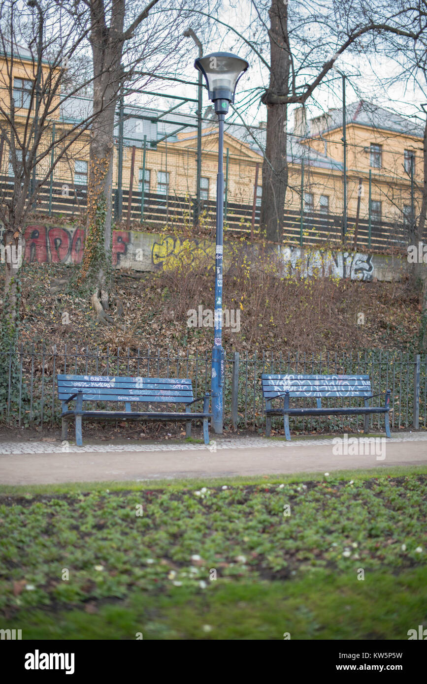 Two park benches and a lamp all completely covered in graffiti with more graffiti on a wall behind Stock Photo