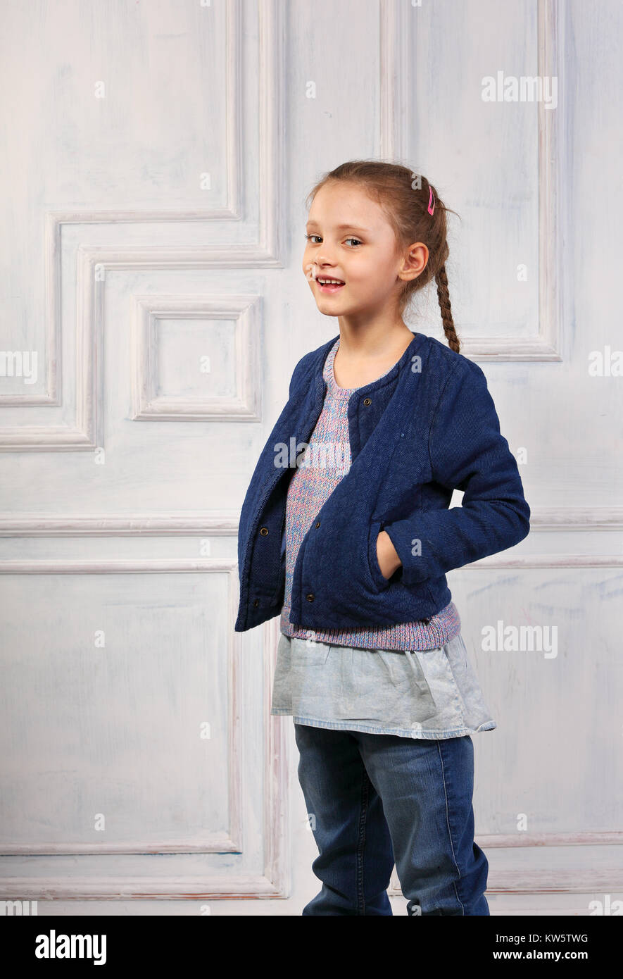 Smiling enjoying cute kid girl in blue jeans jacket on studio blue