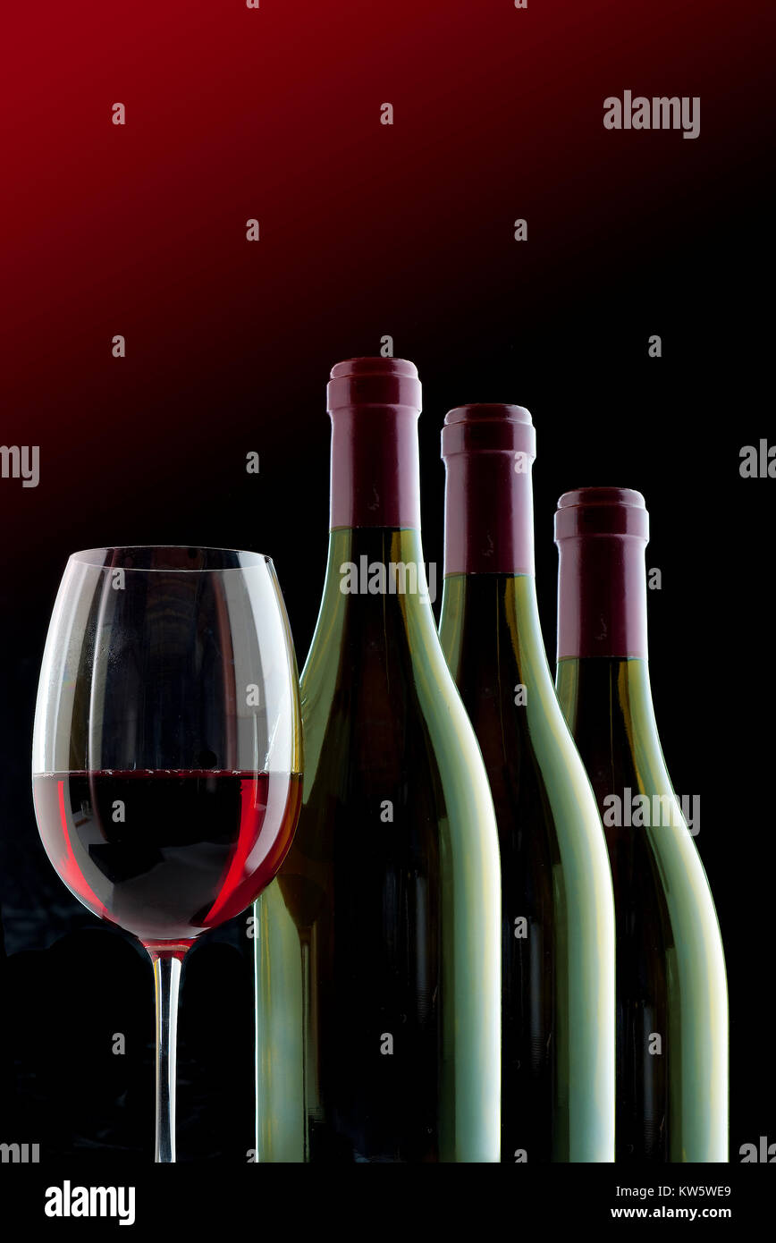 Red wine crystal glass and three wine bottles Stock Photo