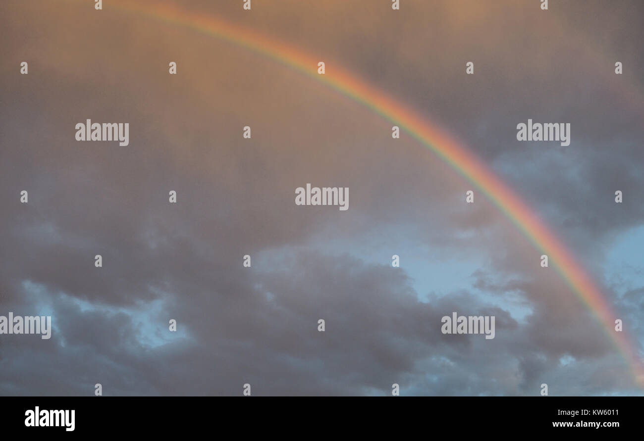 Rainbow in the stormy sky after the rain, lit by the rays of the sun. Stock Photo